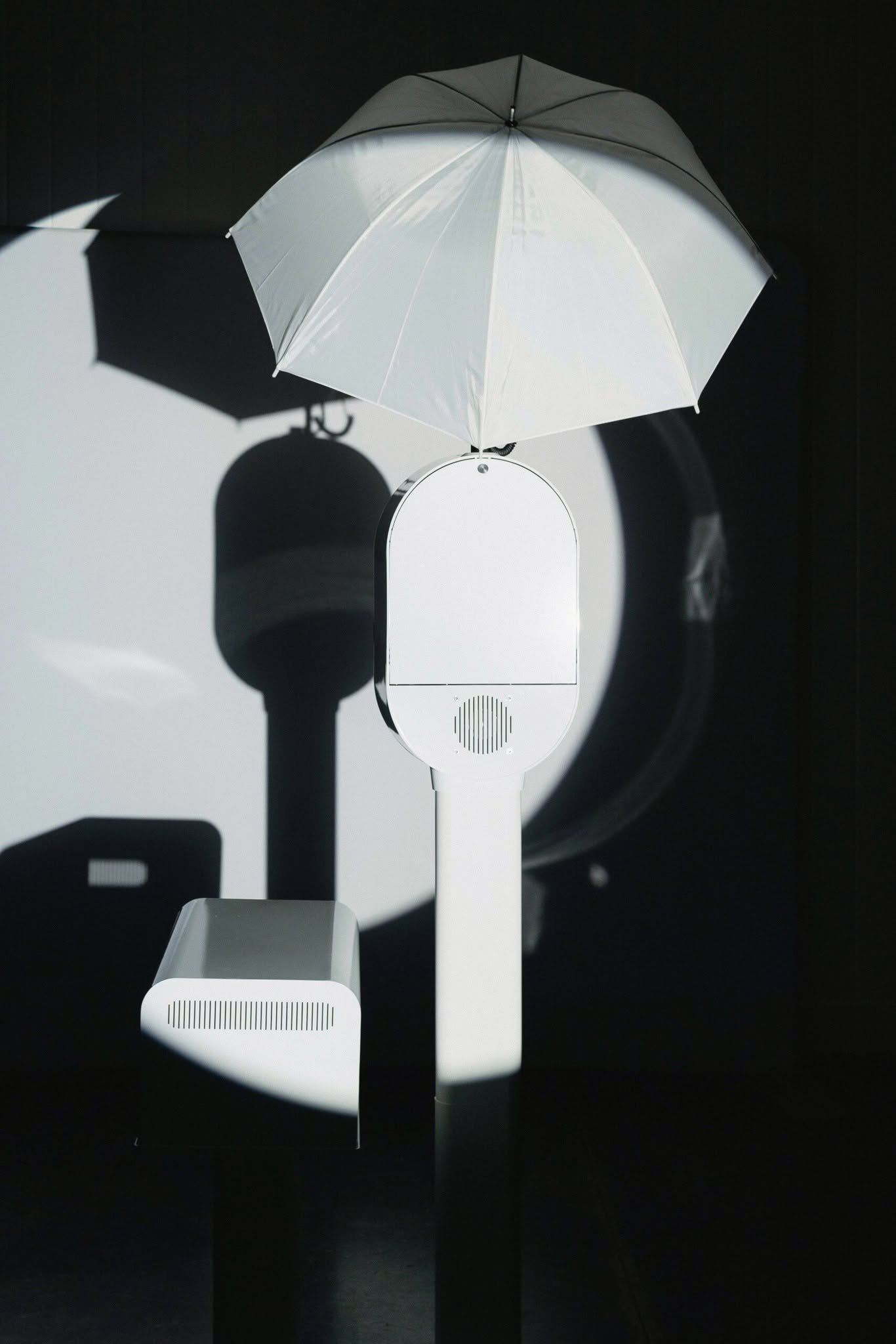 The white photo booth with its umbrella light on a black background.